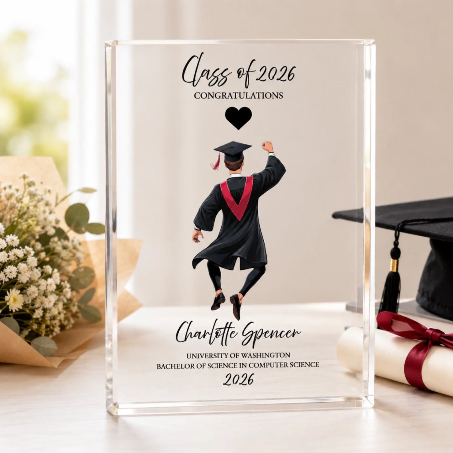 Personalized graduation acrylic plaque for Class of 2026 featuring a female graduate illustration, custom name, university, degree, and year, displayed on a graduation gift table.