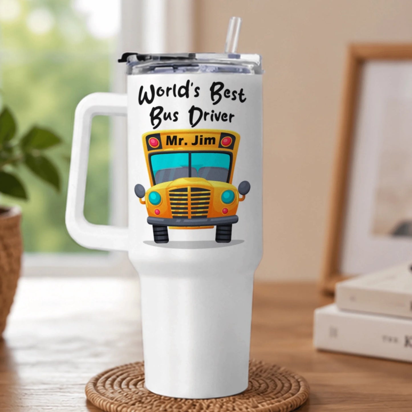 A white handled tumbler with a school bus graphic and "World's Best Bus Driver Mr. Jim" text, rests on a woven coaster.