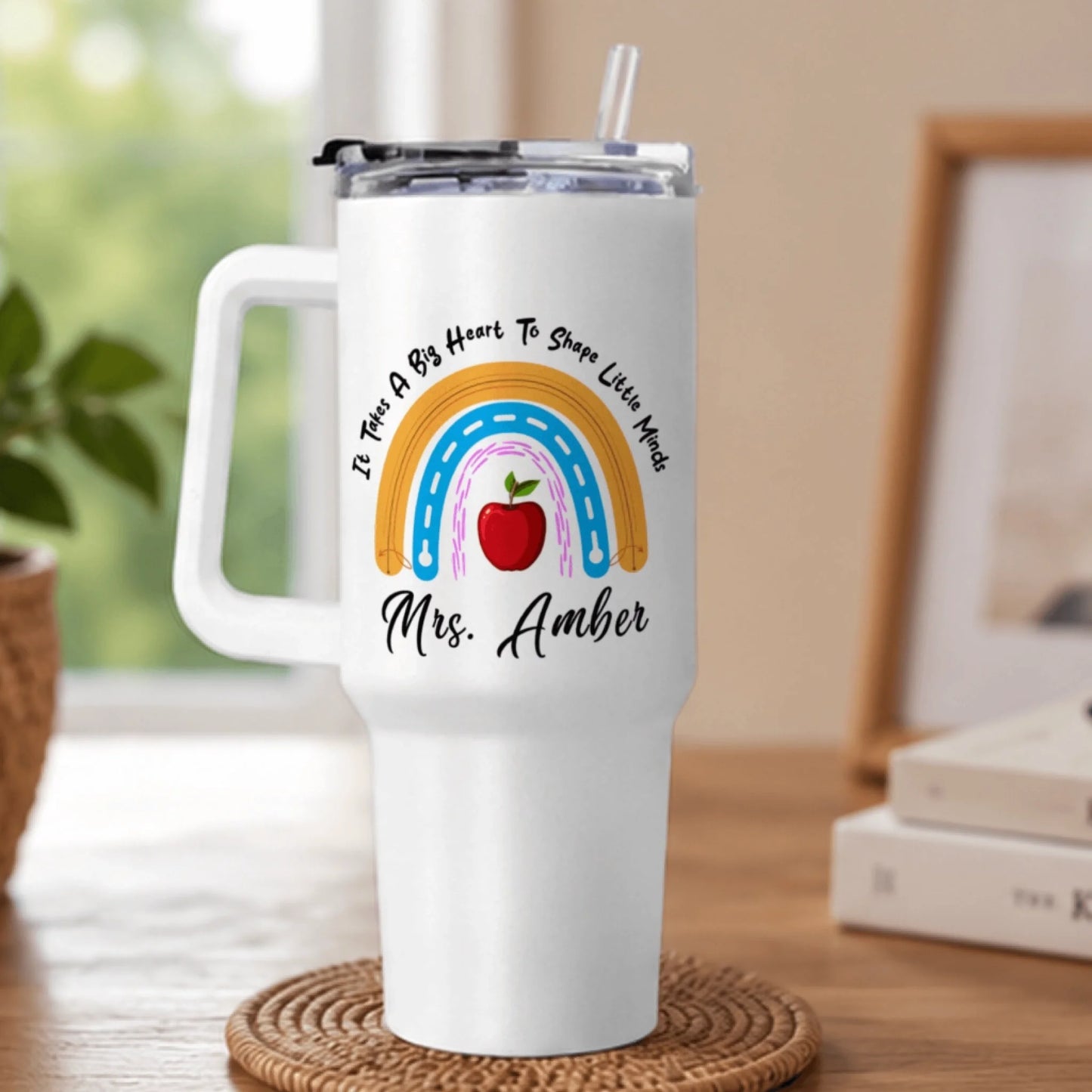 A white handled tumbler with a clear lid and straw, featuring a rainbow design, red apple, and 'Mrs. Amber' text.