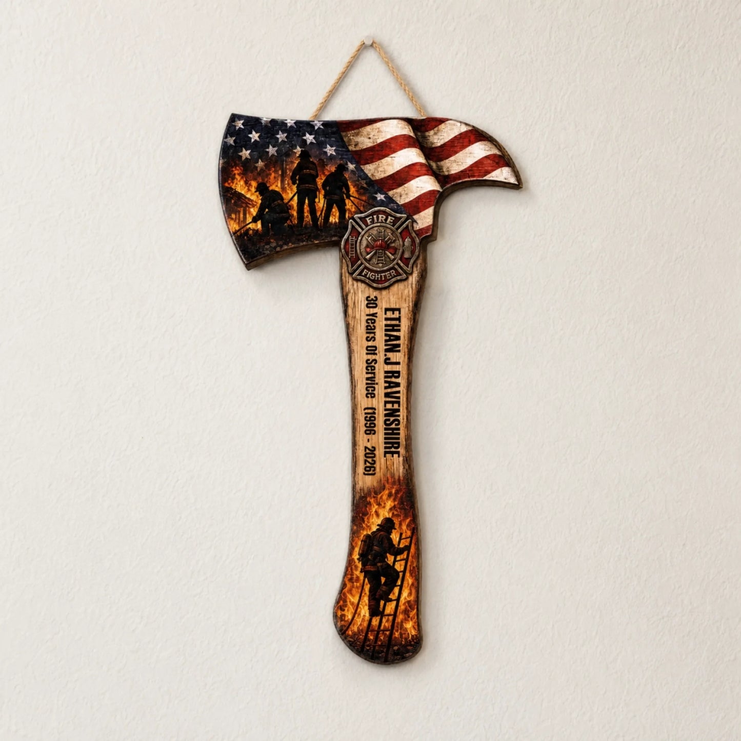 A decorative axe plaque with an American flag, firefighter silhouettes, an emblem, a name, and service dates hangs on a white wall.