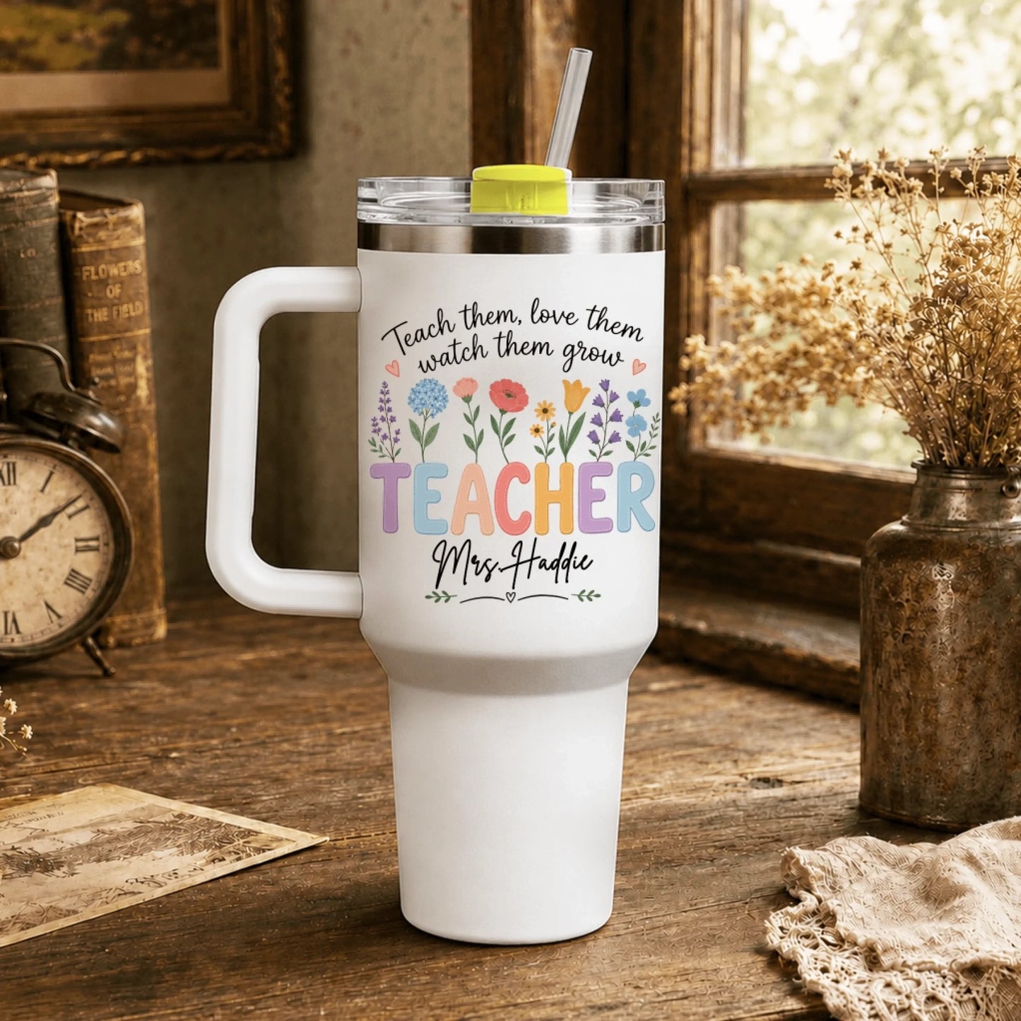 White teacher tumbler with floral design and custom text, placed on a rustic wooden desk next to vintage books.