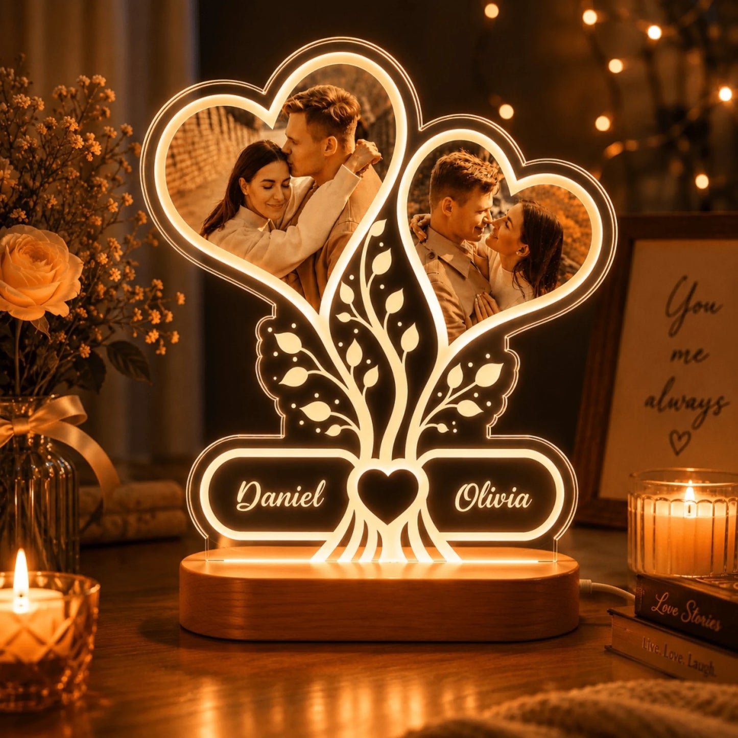 A personalized acrylic night light with two heart-shaped photo frames displaying a couple, a tree motif, and engraved names Daniel and Olivia, set on a wooden base in a cozy room with candles and flowers.