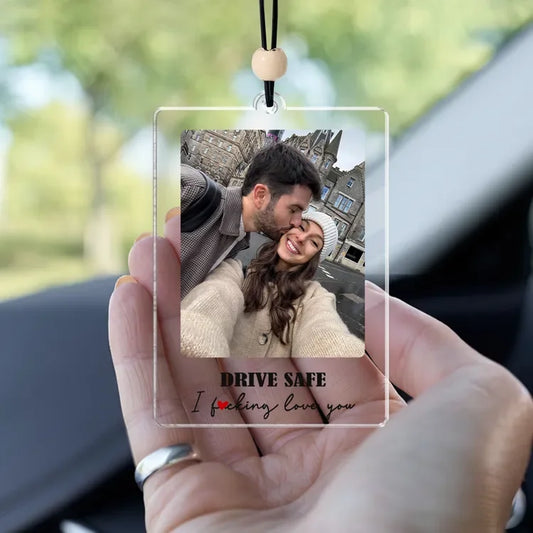 Clear acrylic photo ornament with a couple's photo and 'Drive Safe I love you' text, held in front of a car interior.
