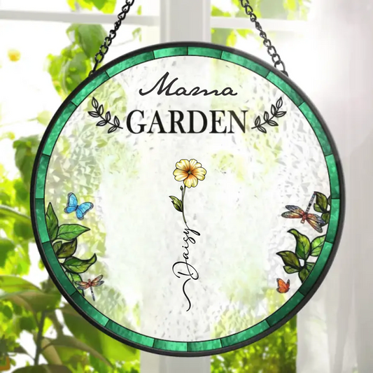 Decorative glass panel with 'Mama Garden' text and floral designs, hanging against a blurred greenery background.