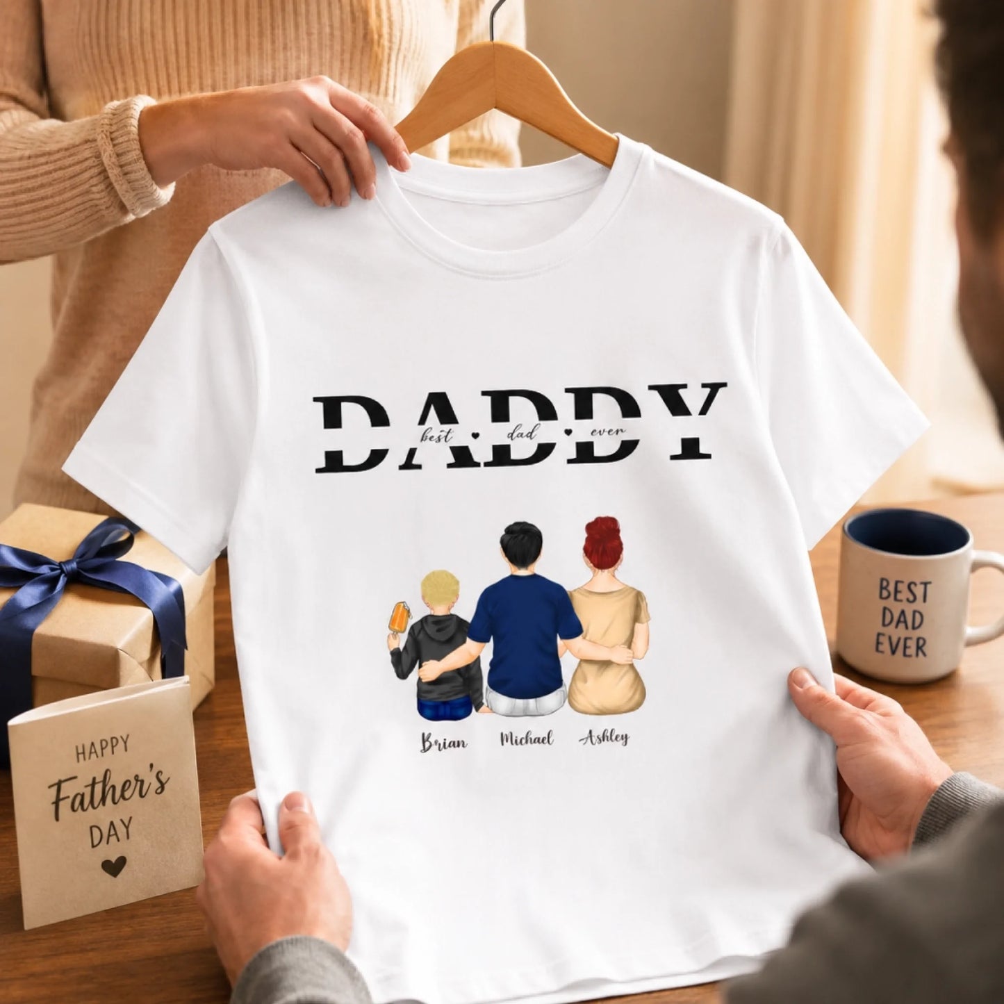 White t-shirt with 'DADDY best dad ever' text and family illustrations, held by a person.