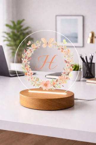 Decorative lamp with floral design and letter 'H' on a table in a cozy room.