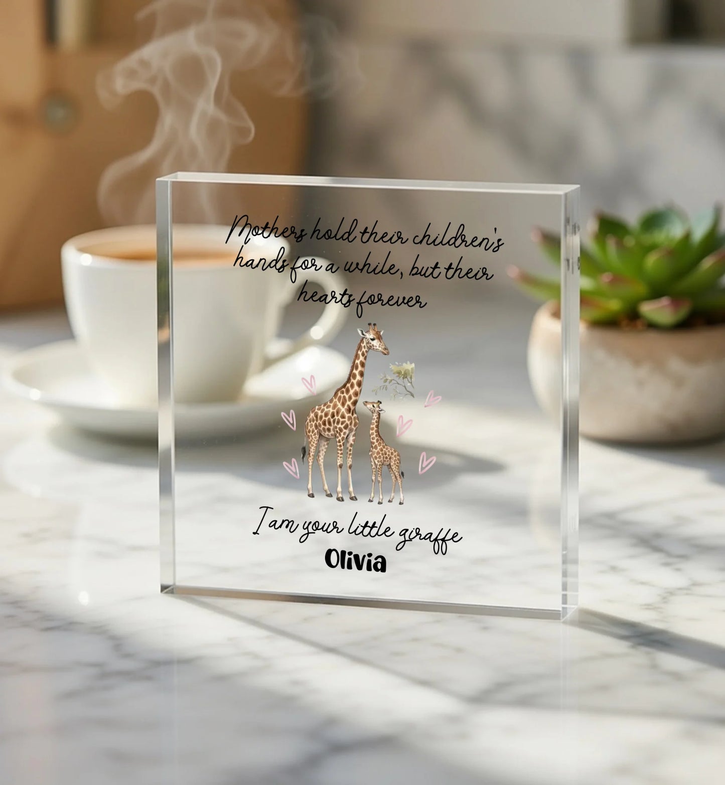 Clear glass block with giraffe illustration and text on a marble surface with coffee and plant.