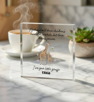 Clear glass block with giraffe illustration and text on a marble surface with coffee and plant.