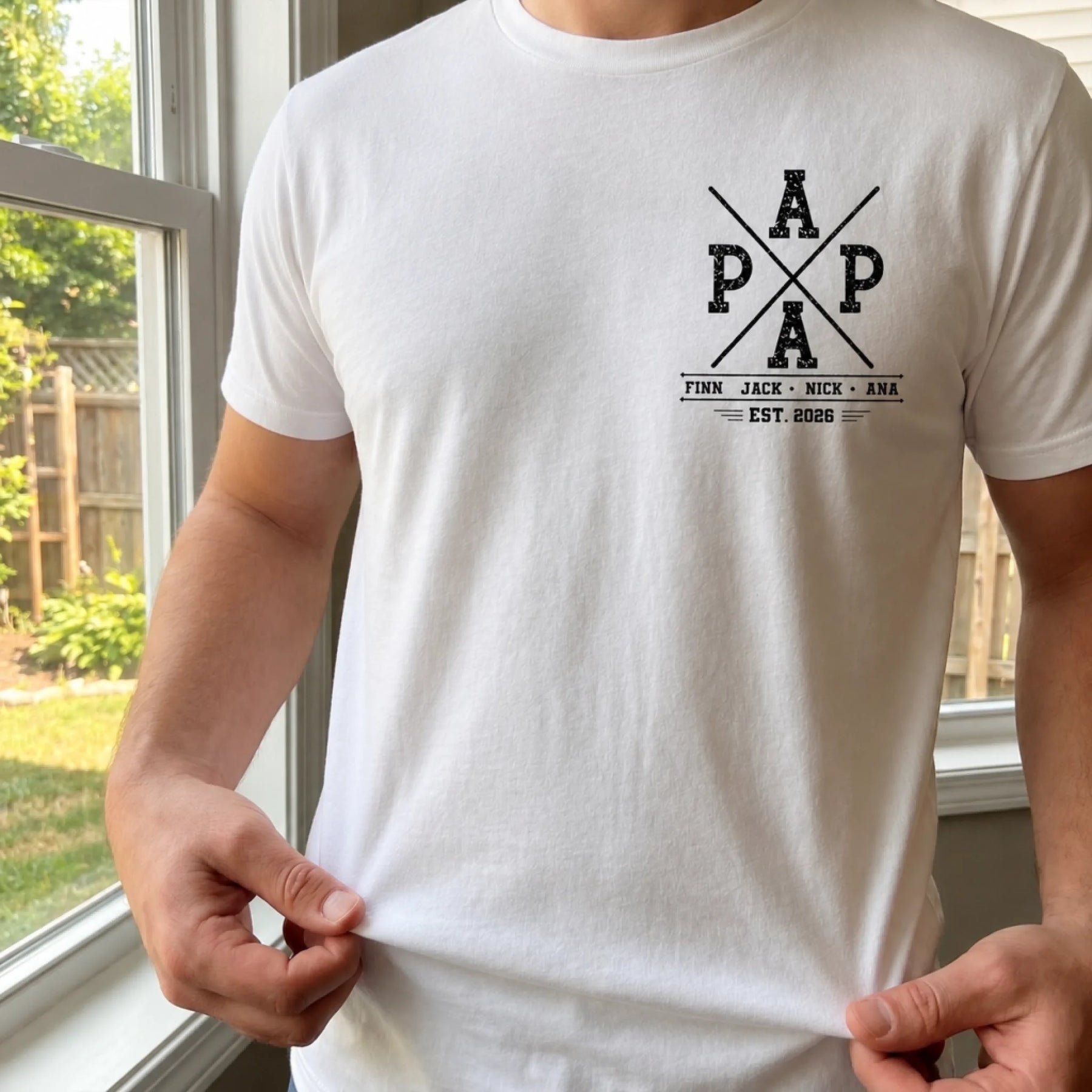 White t-shirt with black graphic design held by a person in front of a window.