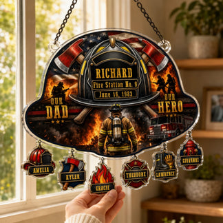 A hand holds a firefighter helmet-shaped suncatcher featuring a flag, helmet, axes, text, and six dangling personalized charms.