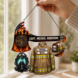 A hand holds an acrylic hanging firefighter ornament shaped like an axe with an American flag, a jacket, helmet, and mask.