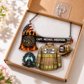 A clear acrylic firefighter-themed hanging plaque, featuring an axe, jacket, helmet, and mask, packaged in an open cardboard box.