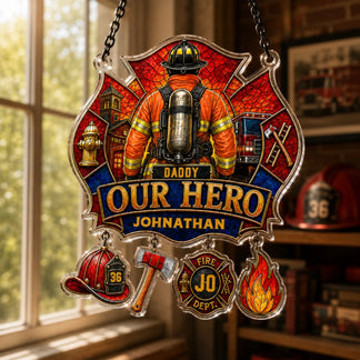 A stained-glass style Maltese cross plaque depicts a firefighter, fire station, truck, "DADDY OUR HERO JOHNATHAN," and charms. Hanging by an indoor window.
