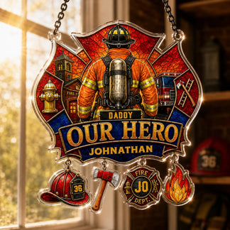 A stained-glass style Maltese cross plaque with a firefighter, "DADDY OUR HERO JOHNATHAN," and charms, hangs in a brightly lit window.