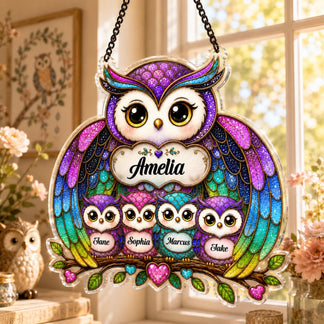A vibrant owl family acrylic hanging sign with glittery, stained-glass style details, depicting a large owl with "Amelia" and four small owls with "Jane," "Sophia," "Marcus," and "Jake" names. It hangs in a sunny window.