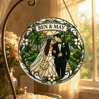 A circular stained-glass style artwork depicting a bride and groom walking arm-in-arm in a vibrant garden. The names 'BEN & MAY' are displayed at the top. It hangs from a metal stand.