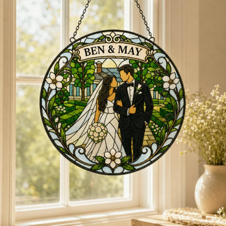 Round stained glass art depicting a wedding couple in a garden scene with a house in the background. A banner at the top reads 'BEN & MAY'.