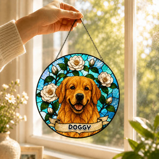 A hand holds up a circular stained-glass style ornament featuring a golden retriever, white flowers, and a 'DOGGY' banner, in front of a sunny window.