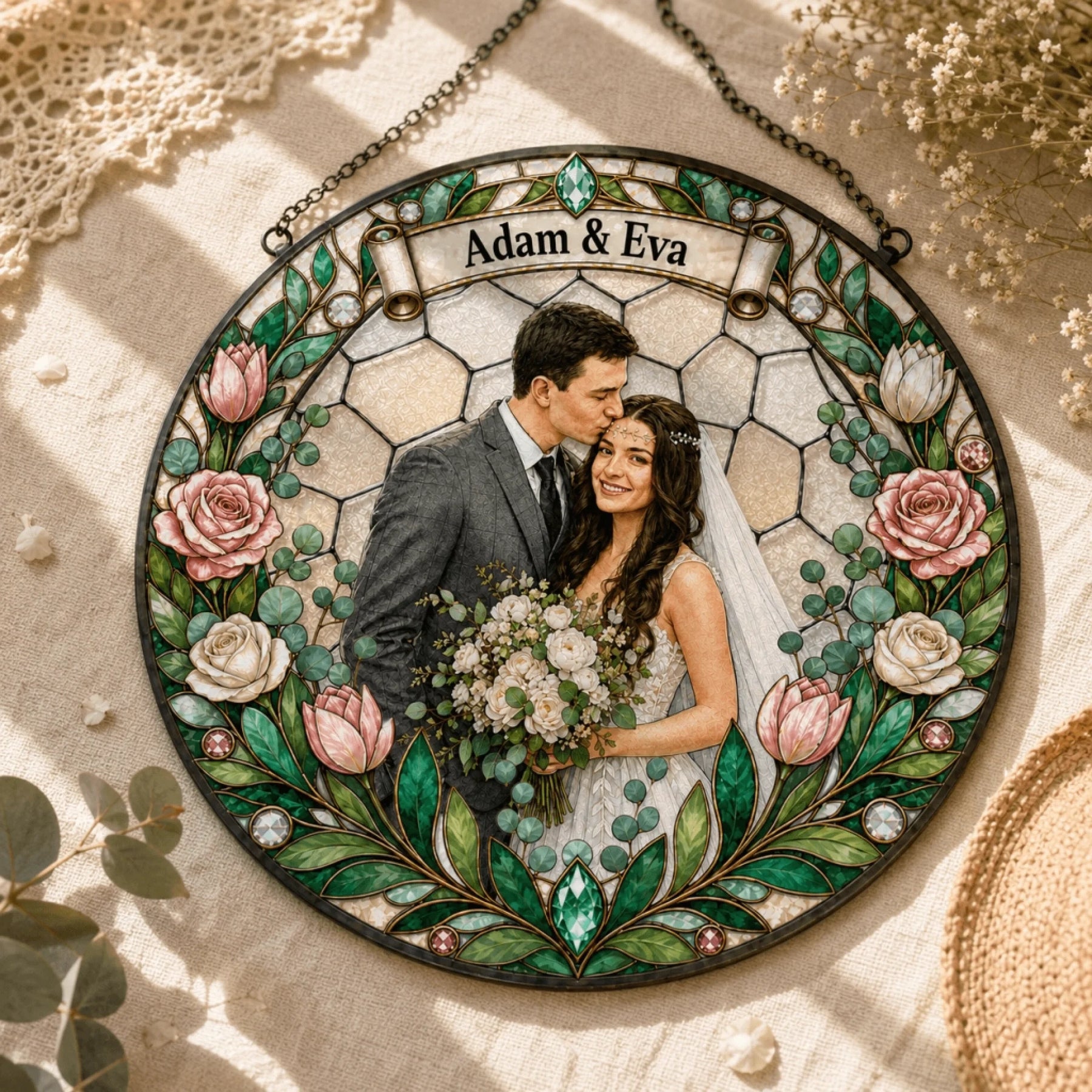 A circular stained-glass-style ornament depicts a man kissing a woman's forehead, surrounded by a floral border and a banner with text.