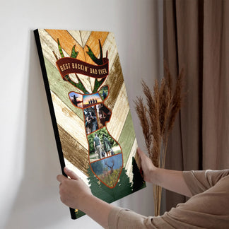 Two hands hold a vertical canvas print featuring a deer head collage with hunting photos and "BEST BUCKIN' DAD EVER" text, against a wall.