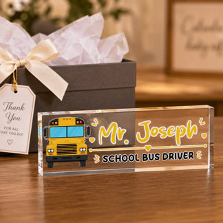 An acrylic desk sign for a school bus driver, featuring a yellow bus and "Mr. Joseph", next to a gift box with a tag.