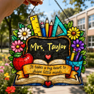 A colorful stained-glass style decorative plaque, featuring "Mrs. Taylor" on a chalkboard, an open book, and supplies, held outdoors.