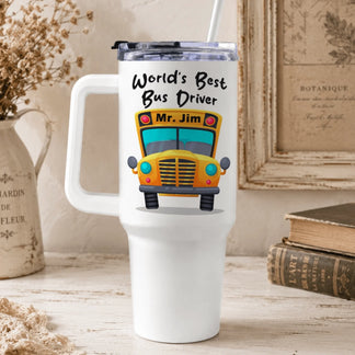 A white handled tumbler, featuring a yellow school bus graphic and "World's Best Bus Driver Mr. Jim" text, sits on a rustic table.