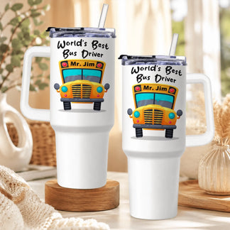 Two identical white handled tumblers, each with a yellow school bus graphic and "World's Best Bus Driver Mr. Jim" text, on wooden surfaces.