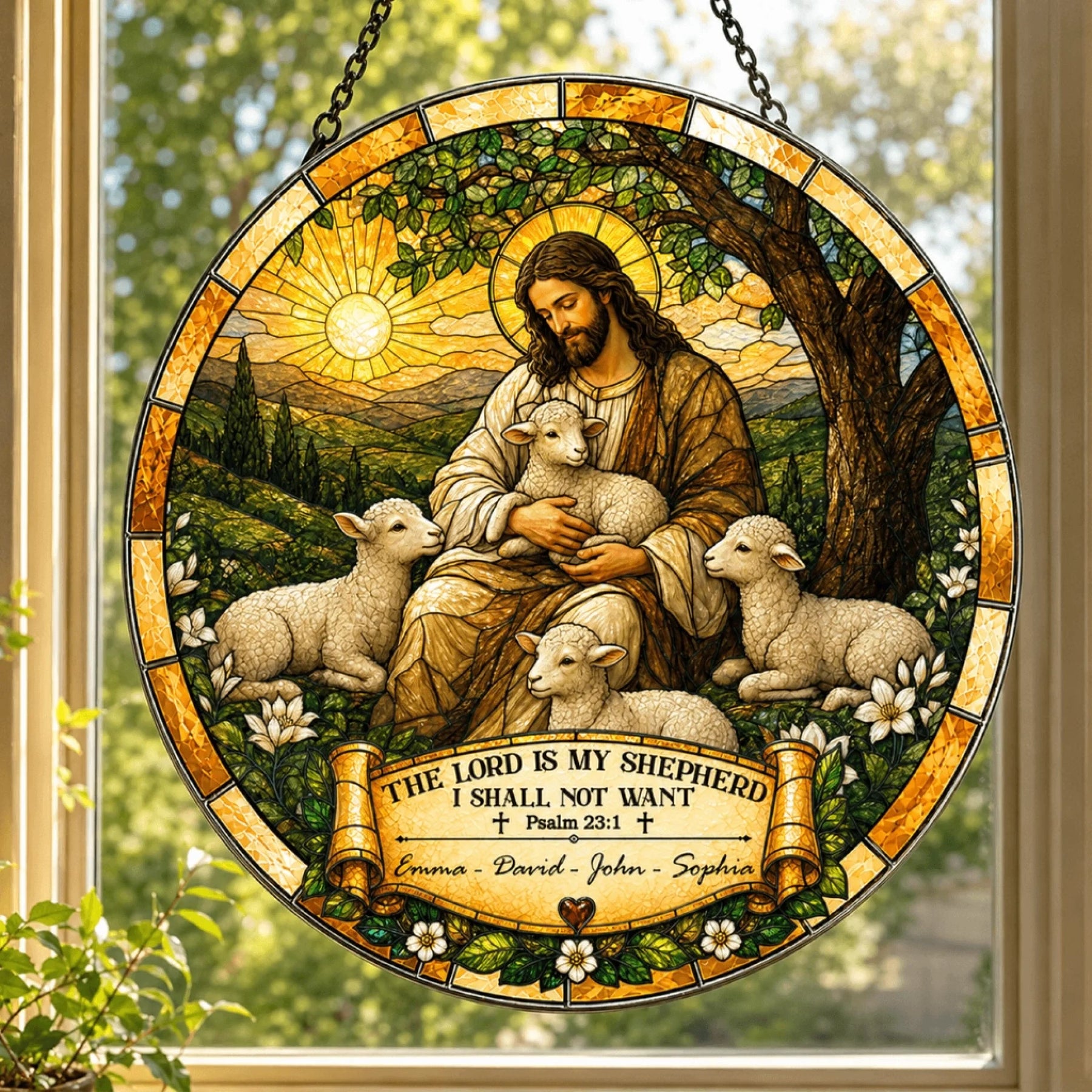 A circular stained-glass style suncatcher hanging in a window, depicting a robed shepherd figure embracing a lamb, surrounded by three other lambs, under a sun. A banner below reads "Emma - David - John - Sophia".
