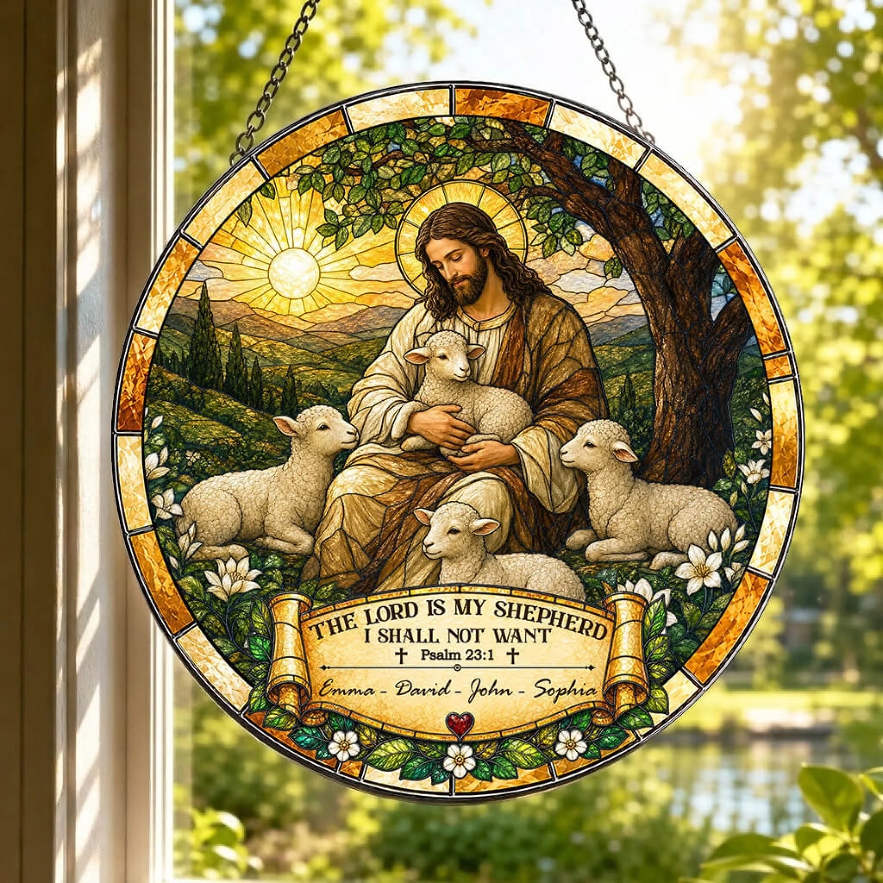 A circular stained-glass style suncatcher, depicting a shepherd figure with lambs, hangs in a window overlooking a pond. A banner reads "Emma - David - John - Sophia".