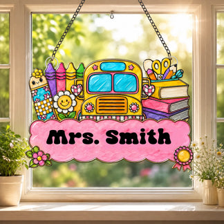 A stained-glass style chalkboard ornament with school supplies, colorful flowers, an apple, and a motivational message, hanging in a sunny window.