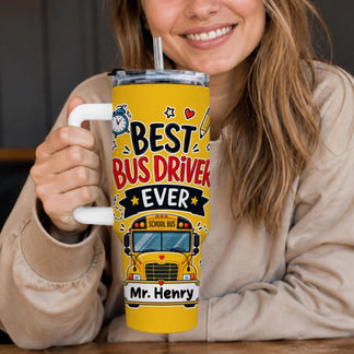 A smiling person in a beige top holds a yellow tumbler with a white handle. It says "BEST BUS DRIVER EVER" with a school bus and "Mr. Henry".