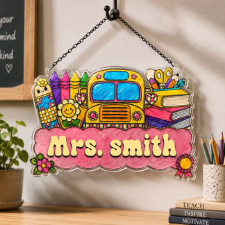 A vibrant school-themed sign featuring a yellow bus, crayons, and books. "Mrs. Smith" is visible on a pink banner.