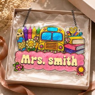 A colorful school-themed decorative sign featuring a yellow bus, art supplies, and books, personalized with "Mrs. Smith," in a gift box.
