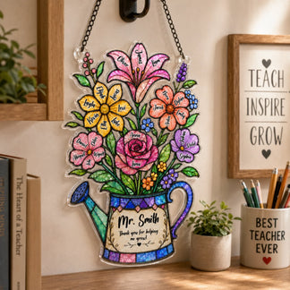 A colorful watering can shaped plaque with flowers, each bearing a name, and a thank you message, hanging on a wall next to a framed inspirational sign.