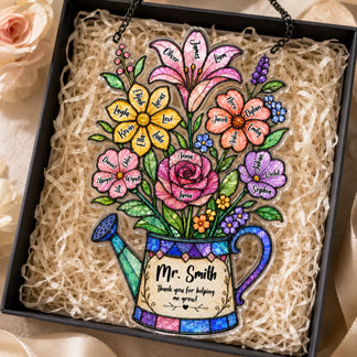 A colorful watering can shaped plaque, filled with named flowers and a thank you message, presented in a black gift box with shredded paper.