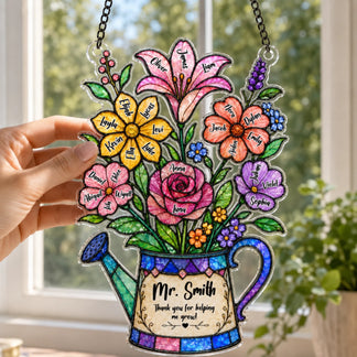 A hand holds up a colorful watering can shaped plaque featuring named flowers and a thank you message, with a bright window in the background.