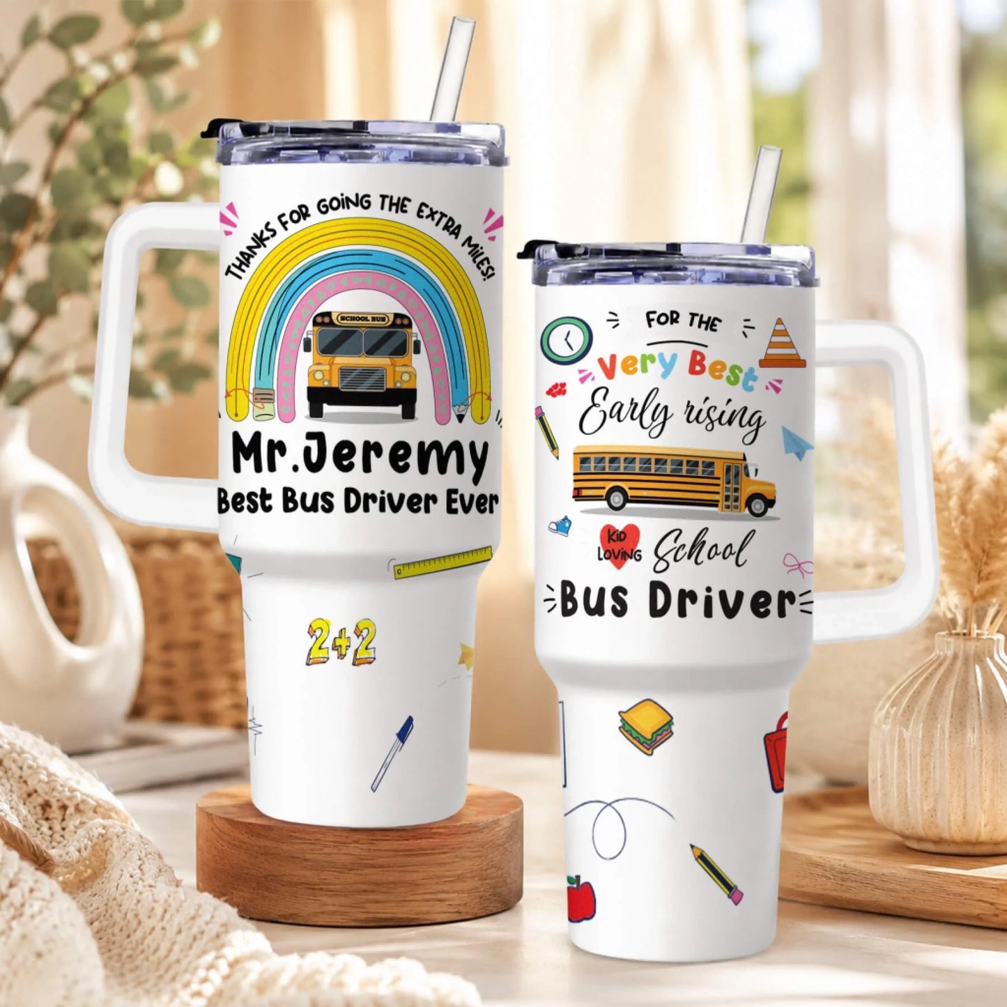 Two white handled tumblers with straws, featuring school bus driver appreciation designs. The left tumbler has a rainbow and school bus.