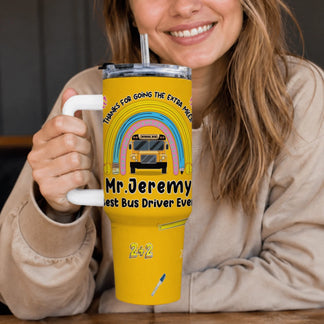 A smiling person holds a yellow handled travel tumbler decorated with a rainbow, school bus, and text "Mr. Jeremy Best Bus Driver Ever".