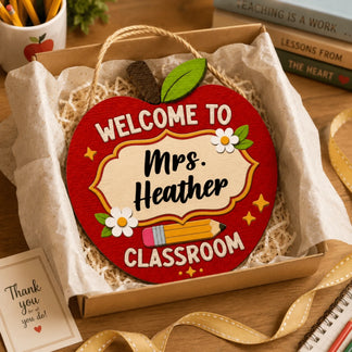 An apple-shaped wooden sign reading "WELCOME TO Mrs. Heather CLASSROOM" with a pencil and flowers, presented in a gift box.