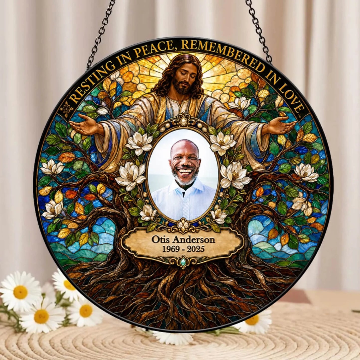 Personalized stained-glass-style hanging memorial plaque featuring Jesus with outstretched arms, white flowers, tree roots, and the text 'Resting in Peace, Remembered in Love,' with a circular portrait photo in the center and the name Otis Anderson 1969–2025 below.