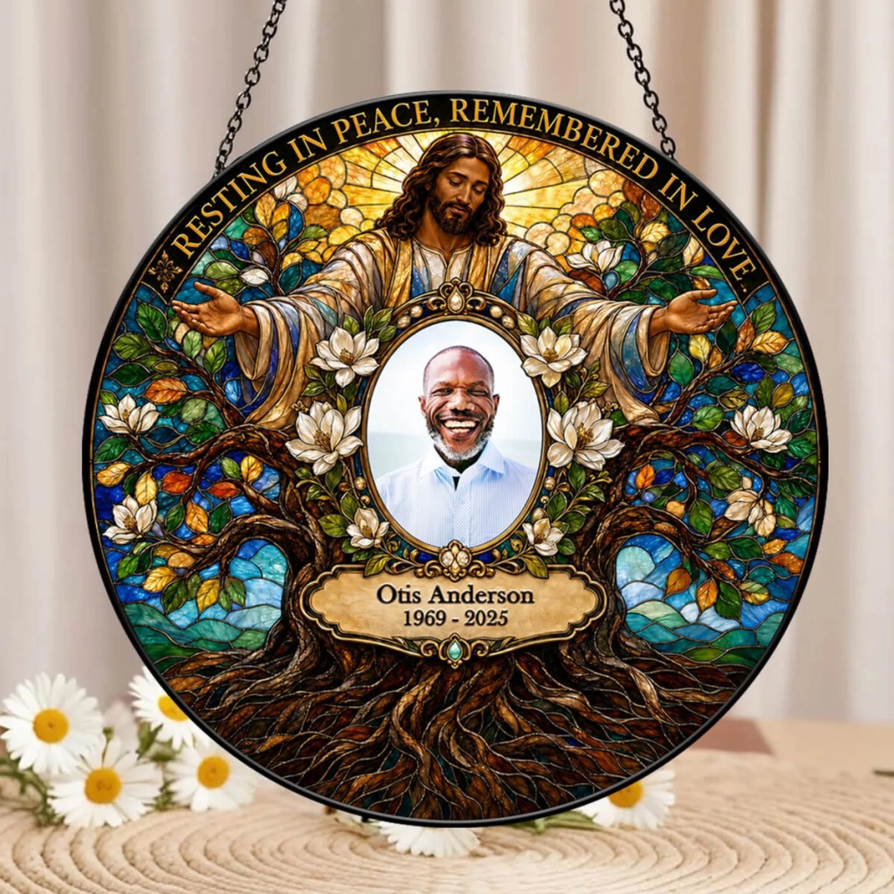Personalized stained-glass-style hanging memorial plaque featuring Jesus with outstretched arms, white flowers, tree roots, and the text 'Resting in Peace, Remembered in Love,' with a circular portrait photo in the center and the name Otis Anderson 1969–2025 below.