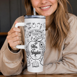 A smiling woman holds a white tumbler with a handle and straw. It's decorated with black line art school doodles and 'Mrs. Taylor'.
