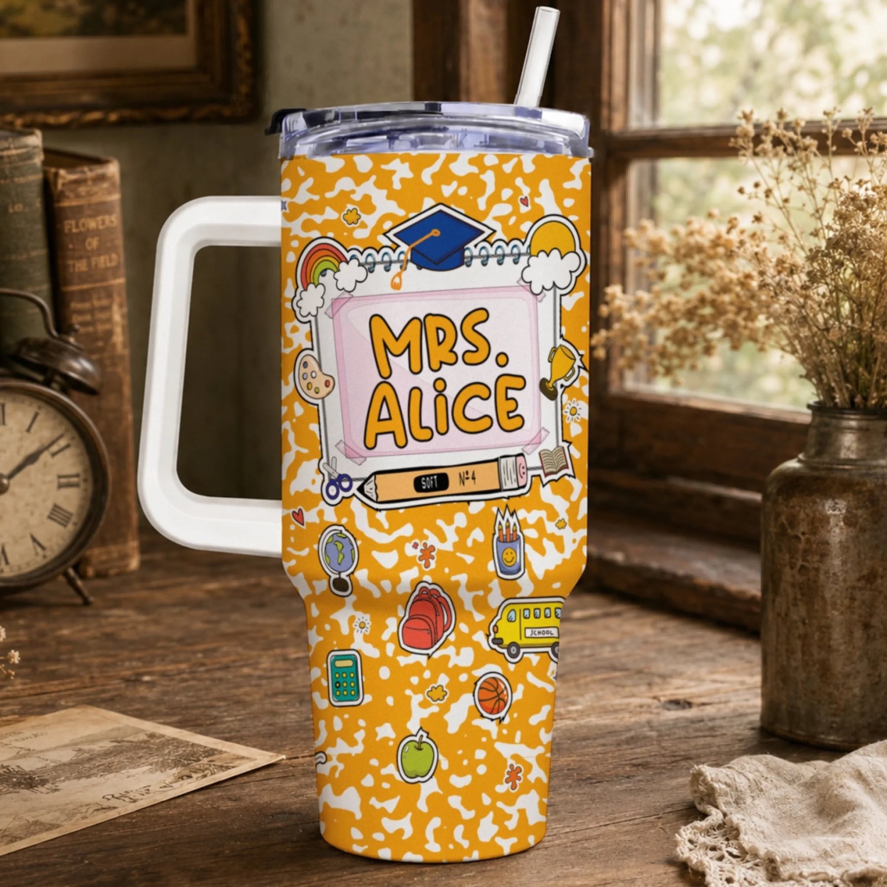 Orange travel tumbler with a white handle, lid, and straw. It features a school-themed design with 'MRS. ALICE' and various colorful illustrations.