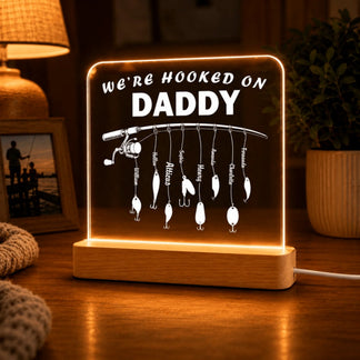 Decorative LED sign with 'We're Hooked on Daddy' text and fishing-themed design on a wooden base.