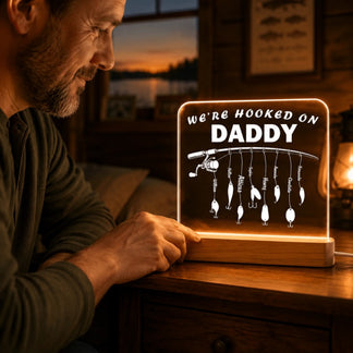 Man holding a personalized light-up sign with fishing lures and 'We're Hooked on Daddy' text.