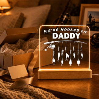 Decorative lamp with fishing lures and text 'We're Hooked on Daddy' on a wooden base.