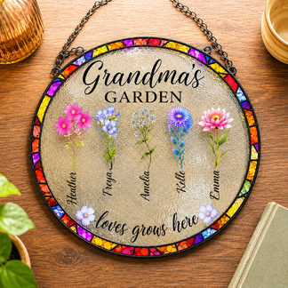 Decorative glass panel with floral designs and text 'Grandma's Garden loves grows here' on a wooden surface.