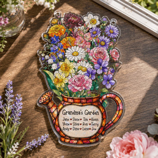A flat, clear acrylic decoration shaped like a watering can filled with a bright array of flowers and a 'Grandma's Garden' label, displayed on a wooden table.