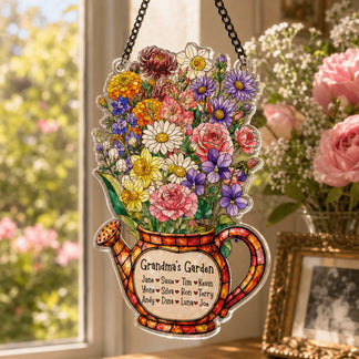 A colorful watering can decoration, overflowing with flowers and a 'Grandma's Garden' label, hangs in a sunlit window beside a lush floral bouquet.